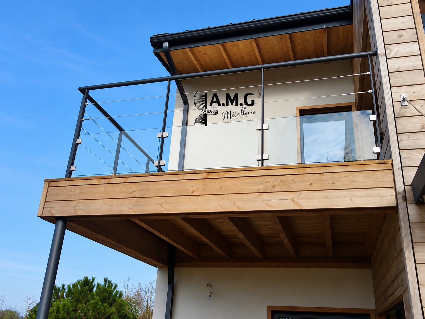 Un balcon en bois équipé d'un garde-corps en métal gris anthracite avec panneaux de verre et câbles inox, sur une maison à bardage bois.