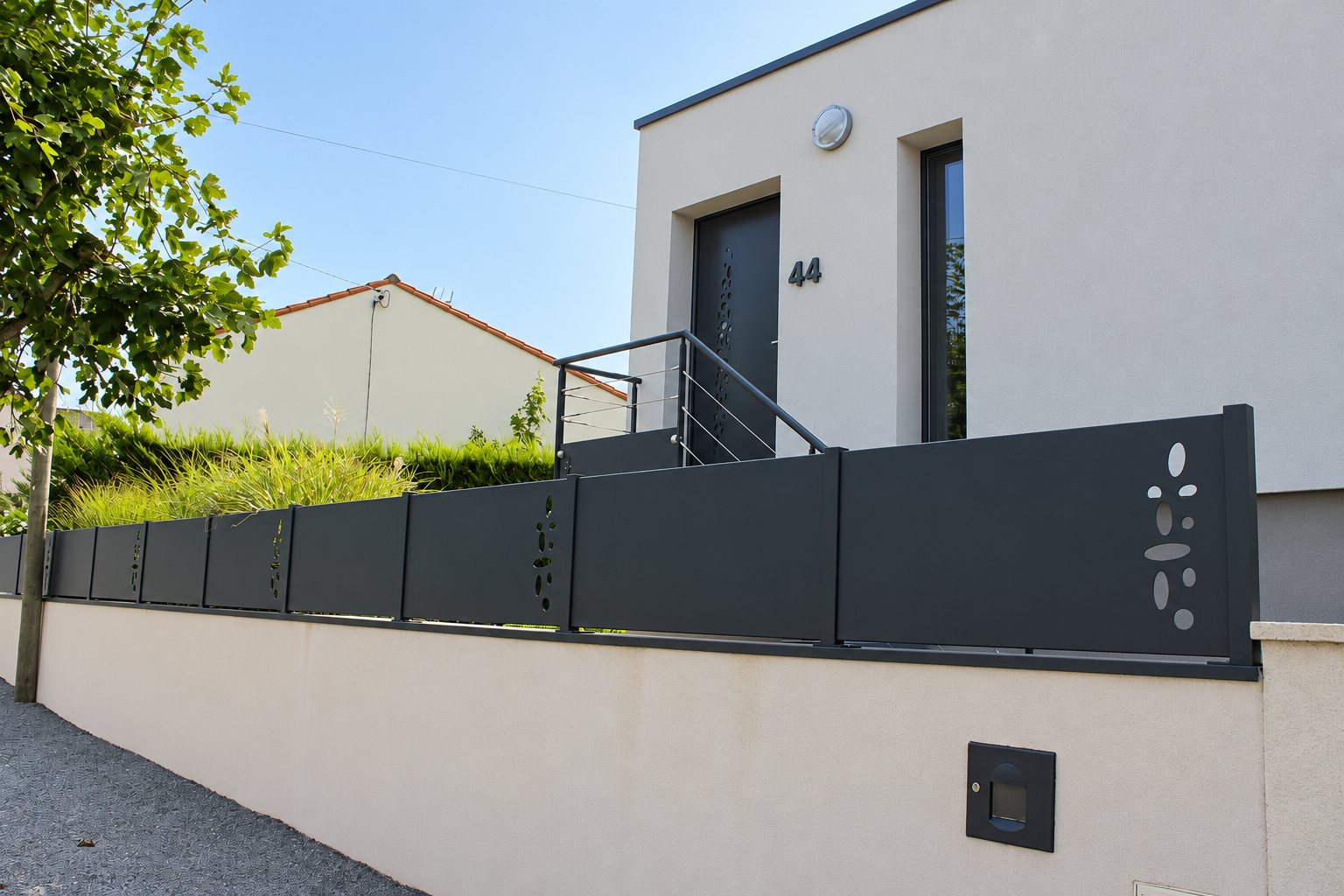 Clôture en panneaux d'aluminium gris anthracite à motifs ajourés posée sur un muret devant une maison moderne au numéro 44.