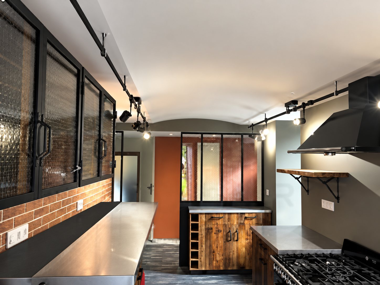 Cuisine moderne de style industriel avec briques, vitrages et plans de travail en inox.