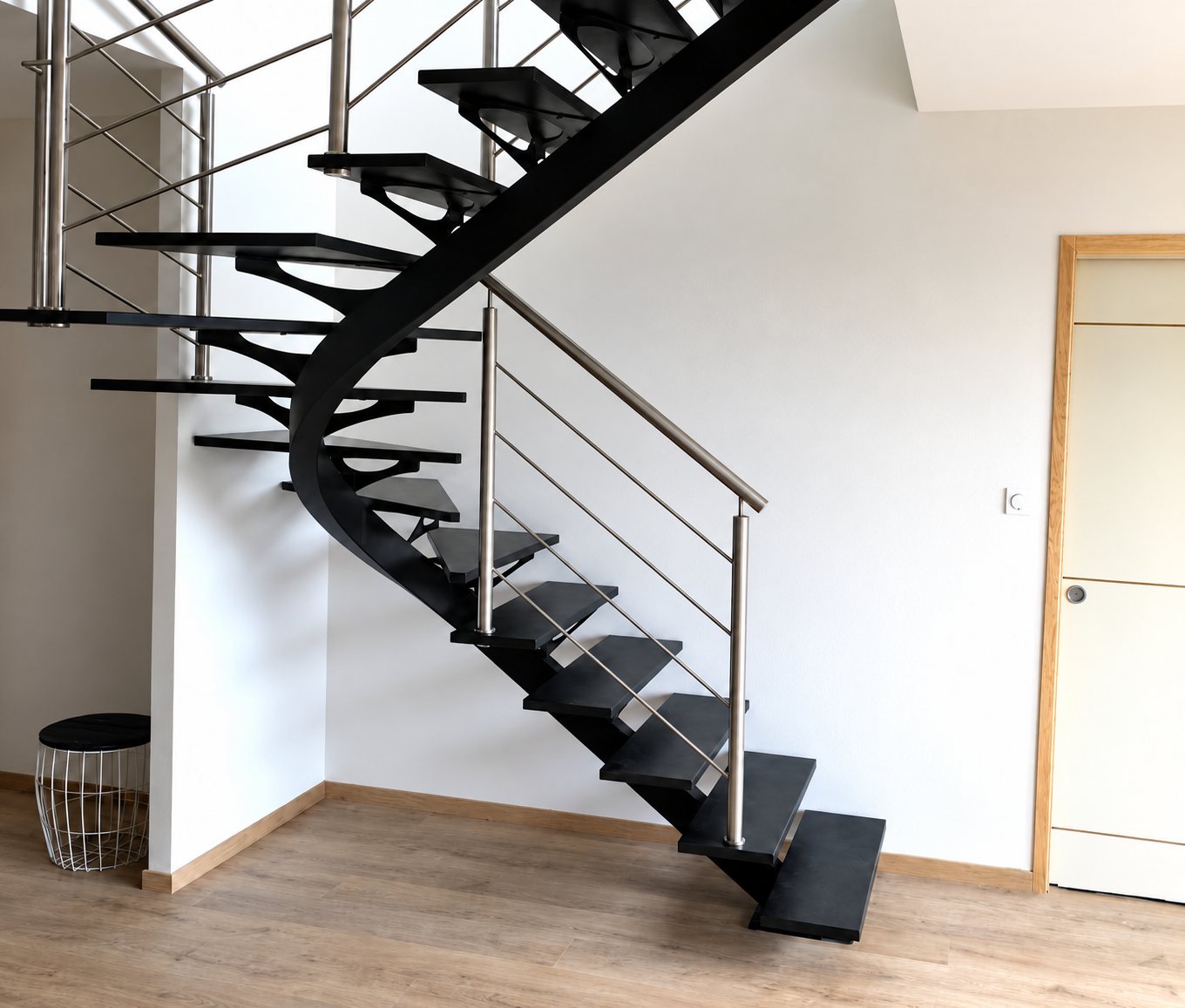 Escalier hélicoïdal noir à limon courbe et rampe en inox dans un intérieur clair.
