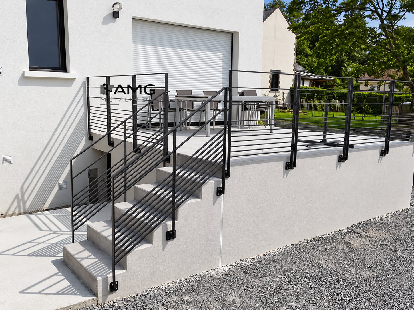 Un garde-corps métallique gris anthracite à barres horizontales borde un escalier en béton et une terrasse surélevée devant une maison blanche.