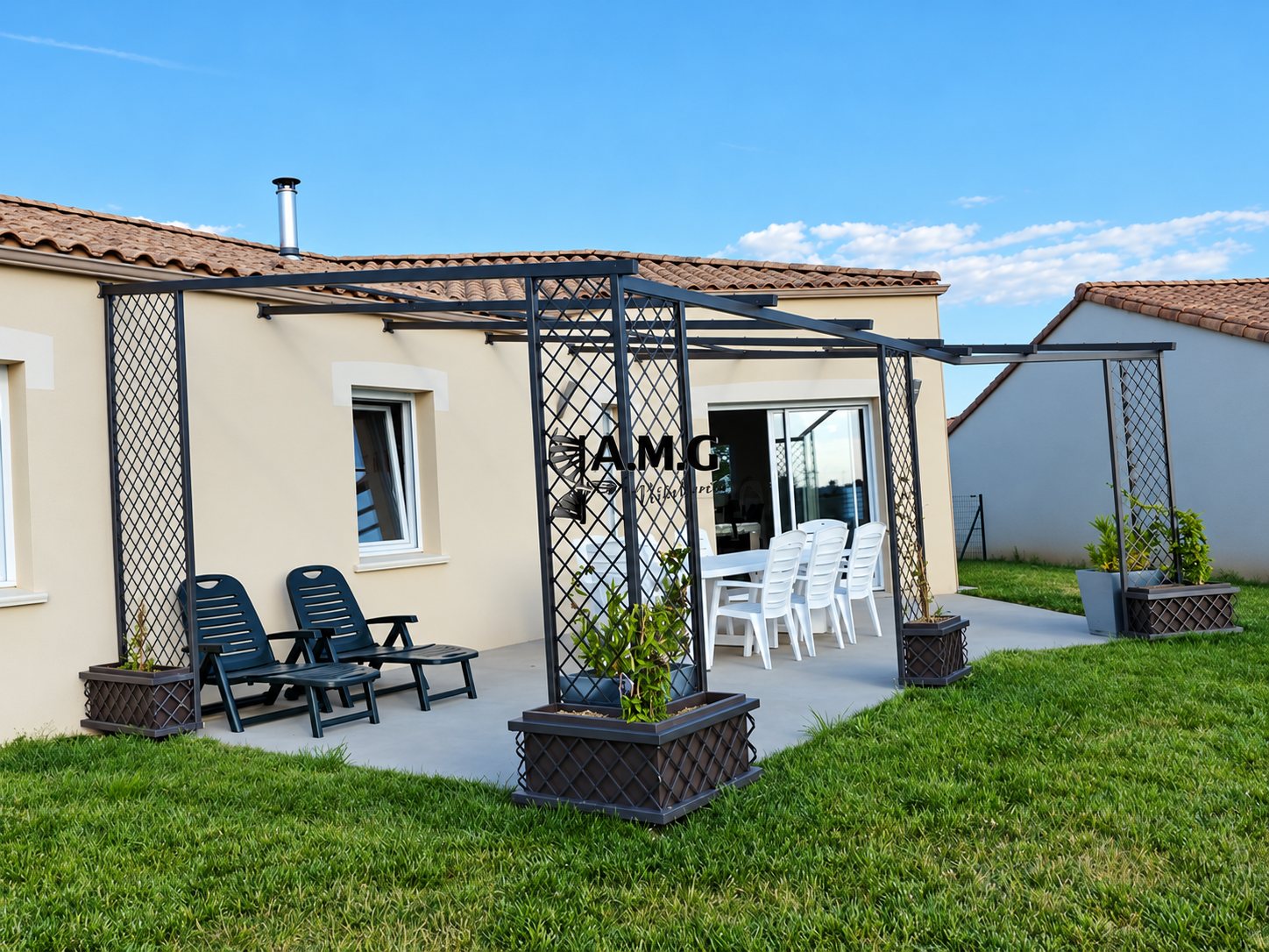 Une pergola en métal gris avec panneaux en treillis et jardinières, installée sur une terrasse en béton devant une maison beige, avec des chaises longues et une table blanche.