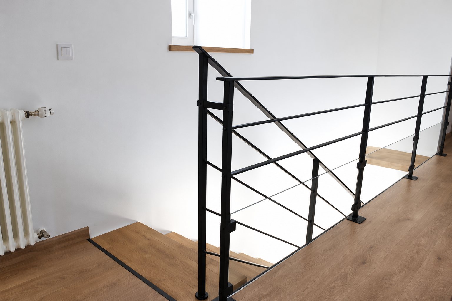Une rambarde en métal noir aux fines barres est installée le long d'un escalier en bois dans une pièce aux murs blancs.